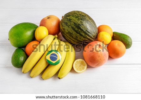 Stack of bananas, oranges and mangos on white wooden table. Brazil flag printed on button badge, export concept.  Royalty-Free Stock Photo #1081668110