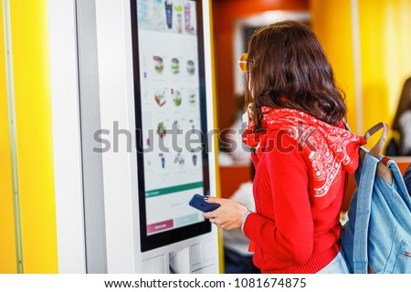 Hipster asian woman orders food at the touch screen self service machine by the electronic menu in the fastfood restaurant Royalty-Free Stock Photo #1081674875