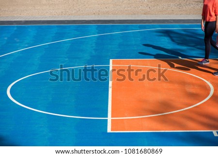 Abstract, blue background of newly made outdoor basketball court in park. Visible asphalt texture, freshly painted lines. Shadow of basketball player, throwing ball in the basket 