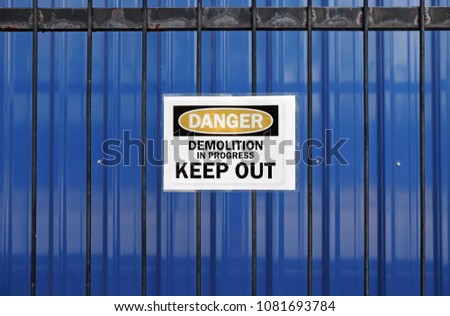 A warning sign on a metal grille fence with the message: Danger, Demolition in Progress, Keep Out. 