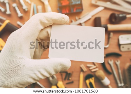 Worker holding blank business card as copy space over workshop table with maintenance and fix-up project tools