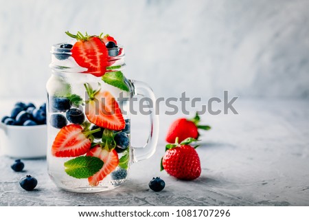 Infused detox water with blueberry, strawberry and mint. Ice cold summer cocktail or lemonade in glass mason jar