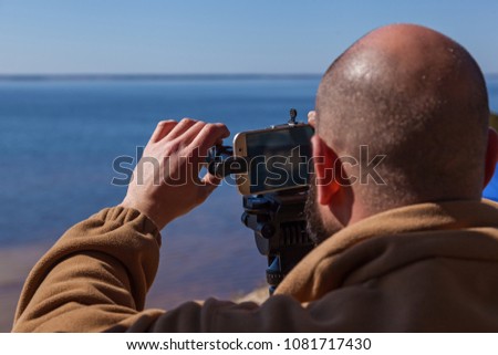 A man adjusts the smartphone on a tripod with lenses. The photographer travels taking pictures of the landscape using a mobile phone