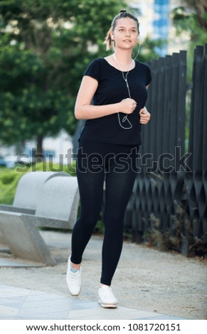 Sporty svelte girl jogging during outdoor daily workout with music