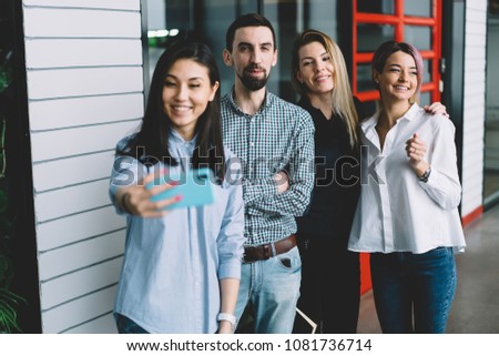 Diversity group of good looking emotional employees dressed in trendy clothes taking together picture on cellular.Prosperous hipster guys making selfie on smartphone camera while standing in office