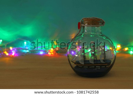 nautical concept image with sail boat in the bottle and multicolor garland lights over wooden table. Selective focus