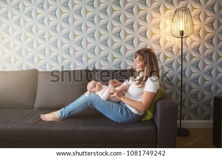 Beautiful young woman with her adorable little baby on the bed at home. Young mother kissing her newborn girl. Mother and infant having good time