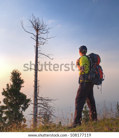 The image of a young man standing at the top of the mountain and looking at the high mountain peaks at sunset, Kazakhstan.
