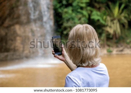Woman tourist standing near waterfall and making picture on smart phone.Woman making selfie near waterfall.Vacation,holiday concept.