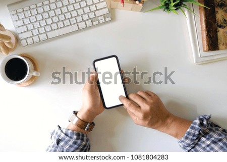 Man using blank screen smartphone on white office desk and office supplies.