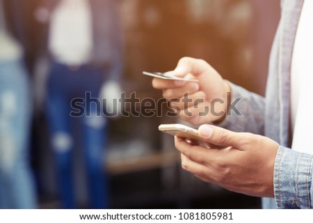 Close up young man hands holding paying with credit card and using cell, smart phone for online shopping Instead of using money Standing in front of a clothing shop store. 