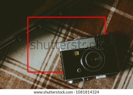 Vintage analogue film camera on a table, old book texture with red frame for text.  Copy space.