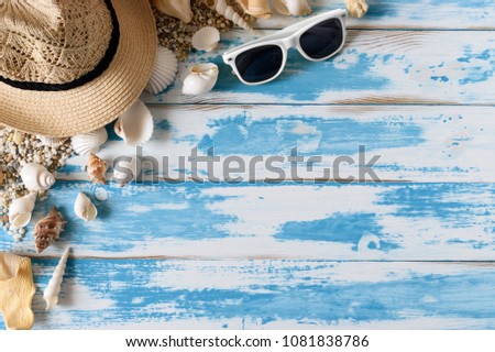 Seashells on blue wooden board with straw hat and sunglasses. Summer holiday background.
