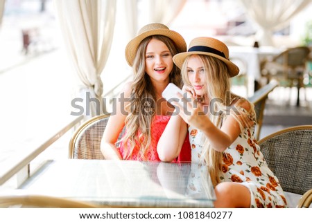 Lifestyle sunny image of best friend girls taking selfie on mobile phone, crazy emotions , happy vacations, shopping day. Wearing elegant dress, way hairstyle, and hats.