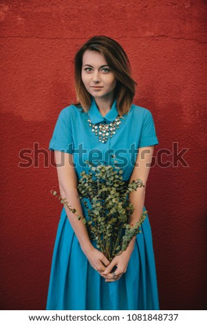 beautiful young brunette girl in blue dress with green flowers on a textured red background