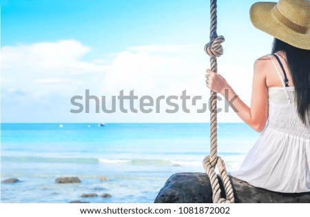 Asia woman traveler sitting on the sing and happy on the beach.beautiful Lady tourist in white dress enjoying for view of the sea on holiday 