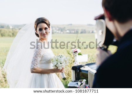 Groom making photo of beautiful bride in wedding dress on the old vintage, retro camera. Wedding photoshoot. Rear view