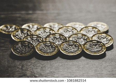 Pound coins lined up in a repetitive pattern on a wooden table top. Queens head and tails shown on silver and gold metal