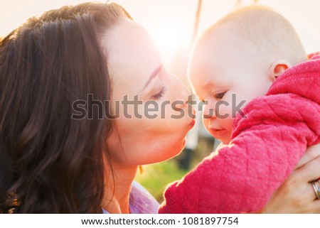Mom kisses the baby in the nose. Mom holds a son in her arms. Sunny evening in the street