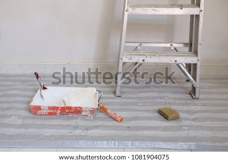 Paint roller and paint brush in paint tray with white color in the tray And there is a staircase beside it.