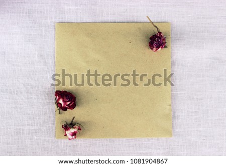 Romantic composition with purple dry rose buds and paper blank on textile linen background. Concept for greeting card for valentine or birthday. Love theme.Shabby chic