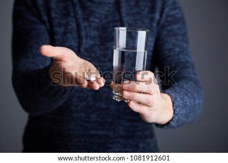 A man is holding a glass with effervescent tablet dissolved  in the gass of water. Aspirin is in the glass of water