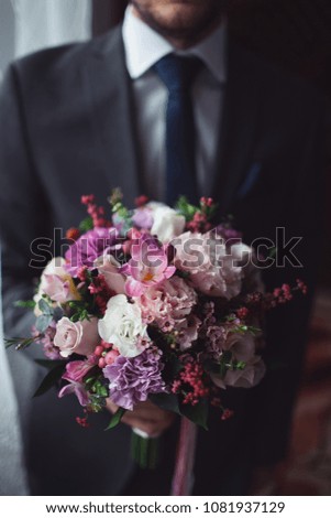 the groom in a dark jacket holds a bouquet of a bride from pink and white flowers
