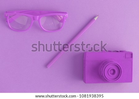 Flat lay of eyeglasses, pencil and retro film photo camera. Purple colored background concept.