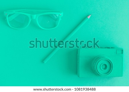 Flat lay of eyeglasses, pencil and retro film photo camera. Green colored background concept.