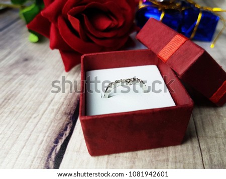 A ring in red box with red rose on wooden background