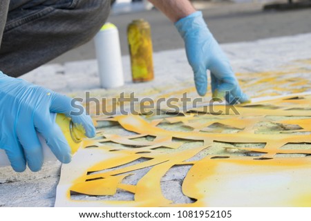 The process of creating a street art on the sidewalk. The artist paints an ornament using paint brush and aerosol. modern urban culture Royalty-Free Stock Photo #1081952105