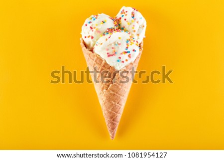 ice cream balls with colored sugar sprinkles in a Waffle Cone on a yellow Background. Vanilla ice cream in a waffle cone. Royalty-Free Stock Photo #1081954127