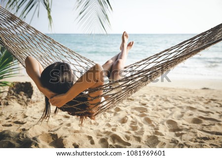 Summer vacations concept, Happy woman with white bikini, hat and shorts Jeans relaxing in hammock on tropical beach at sunset, Koh mak, Thailand Royalty-Free Stock Photo #1081969601