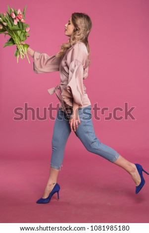 girl is jumping with a bouquet of flowers. blonde is jumping on a pink background