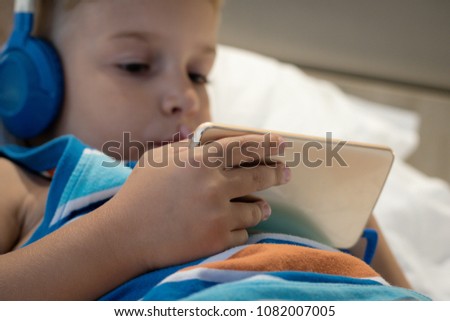 Close up of boy relaxing on bed and using mobile phone for watching something on the internet. 