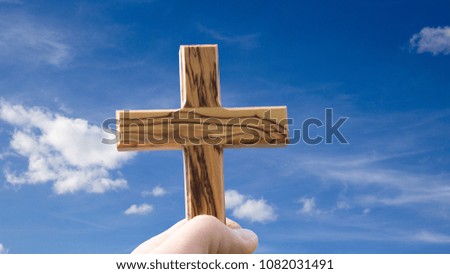 holding wooden christian cross against blue sky
