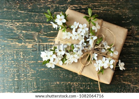 Pretty gift box wrapped with simple brown craft paper and decorated with and branch of tree with white spring flowers. Romantic concept for presents decor. Rustic style, rough green wooden  background
