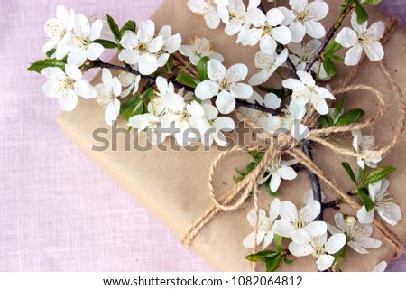 Pretty gift box wrapped with simple brown craft paper and decorated with jute bow and branch of tree with white spring flowers. Romantic concept for presents decor. Rustic style, textile background
