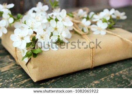 Pretty gift box wrapped with simple brown craft paper and decorated with and branch of tree with white spring flowers. Romantic concept for presents decor. Rustic style, rough green wooden  background