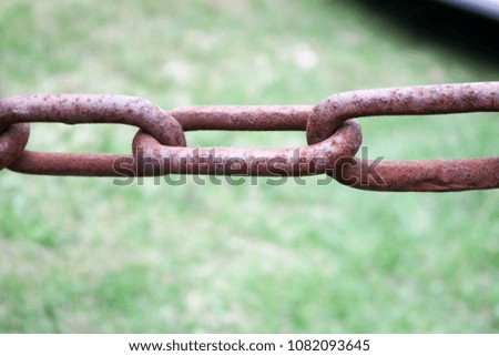 Rusty oxidized red old old strong forged metal iron chain with connected links on the background of green grass