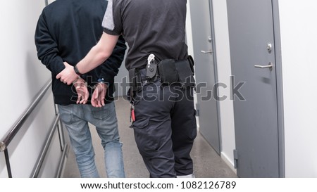 Prison guard escort arrested inmate through jail corridor Royalty-Free Stock Photo #1082126789