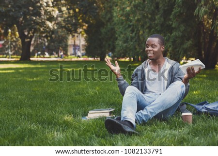 Smiling young african-american man making notes in workbook, got inspiration, sitting on grass in park. Education, inspiration concept, copy space