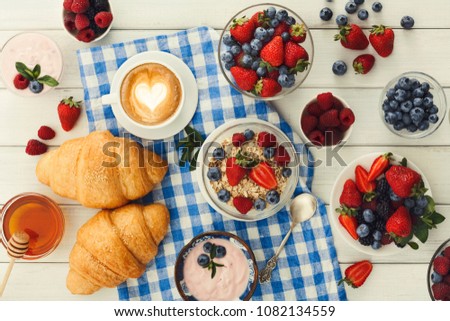 Rich continental breakfast. French crusty croissants, muesli, glass of fresh milk, cup of hot black coffee and lots of sweet berries for tasty morning meals. Delicious start of the day, top view