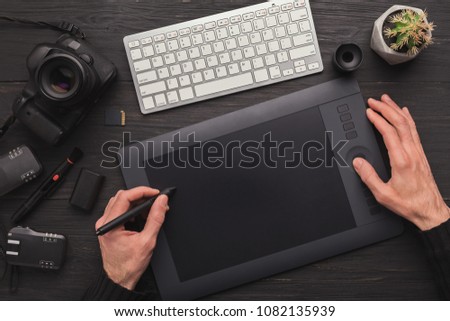 Top view on workplace of photographer. Creative designer hands working with computer keyboard and graphic tablet, photographic equipment on table