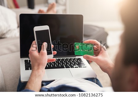 Booking tickets online on laptop and smartphone, holding credit card. Unrecognizable man preparing for vacation, holding device with blank screen travel and modern technologies concept, copy space