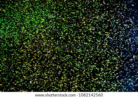 Confetti fired in the air during a beach party. Only confetti on black background of the night. Confetti green, yellow and blue
