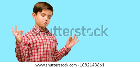 Handsome child with green eyes doing ok sign gesture with both hands expressing meditation and relaxation over blue background