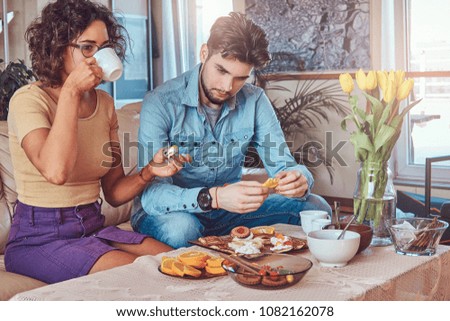 Attractive couple, handsome bearded stylish guy and curly beauty girl eating a meal at home.