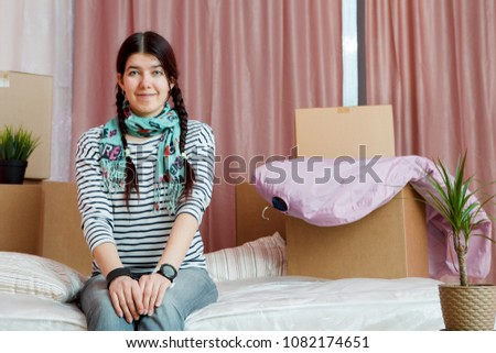 Photo of happy woman sitting on sofa among cardboard boxes