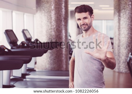 Portrait of young Caucasian sporty man standing in cardio room of modern fitness center and showing high five gesture to camera